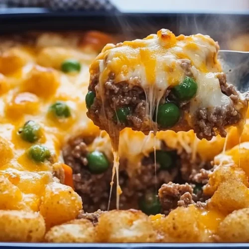 A close-up of a spoon lifting a cheesy, hearty portion of hot dish with golden tater tots